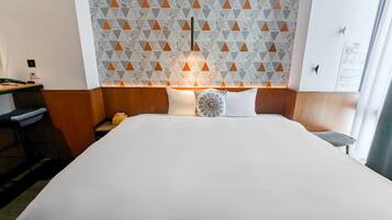 A hotel room with a large bed, a wooden headboard, a patterned wall, and a desk with a lamp.