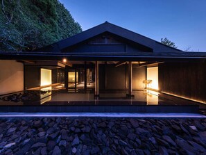 A modern house with a flat roof, large glass windows, and a stone pathway leading to the entrance.