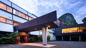 A modern building with a covered entrance and a mountain in the background. - Mifuneyama Rakuen Hotel (Takeo)