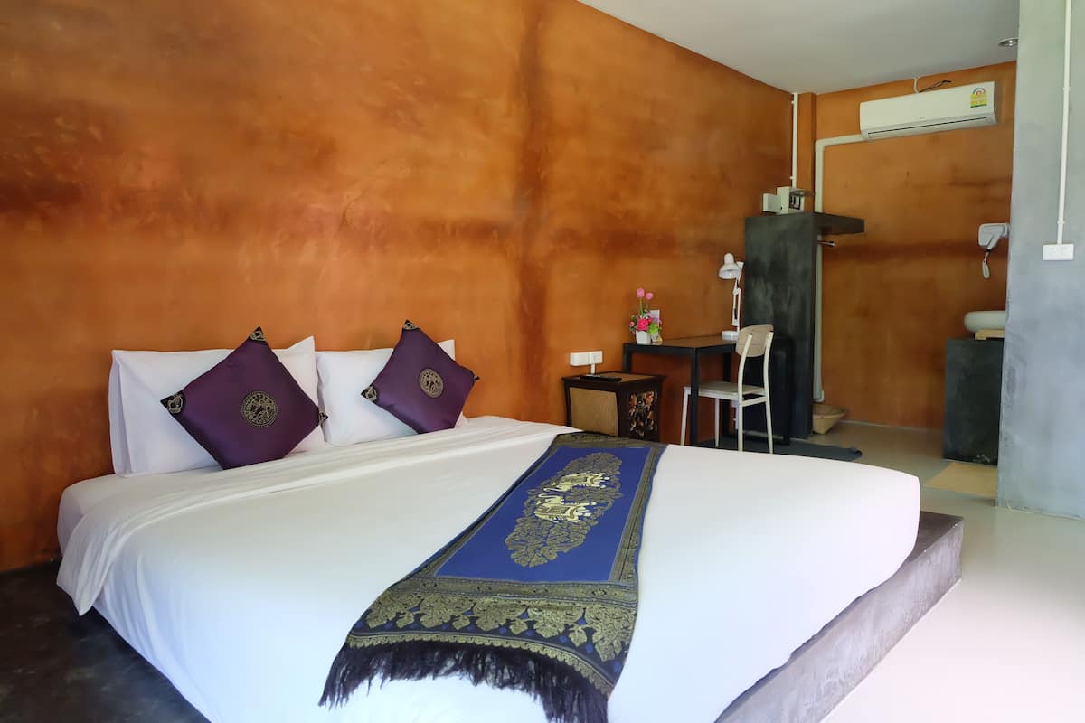 A hotel room with a large bed, orange walls, a desk, and a chair.