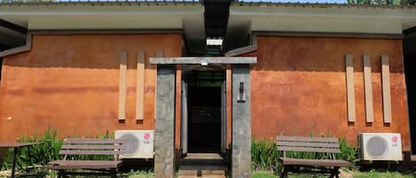 A building with a brown exterior, a central entrance, and two benches with air conditioning units.