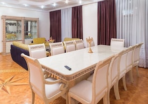 Uma sala de jantar com uma mesa comprida, cadeiras brancas e um candelabro decorativo.