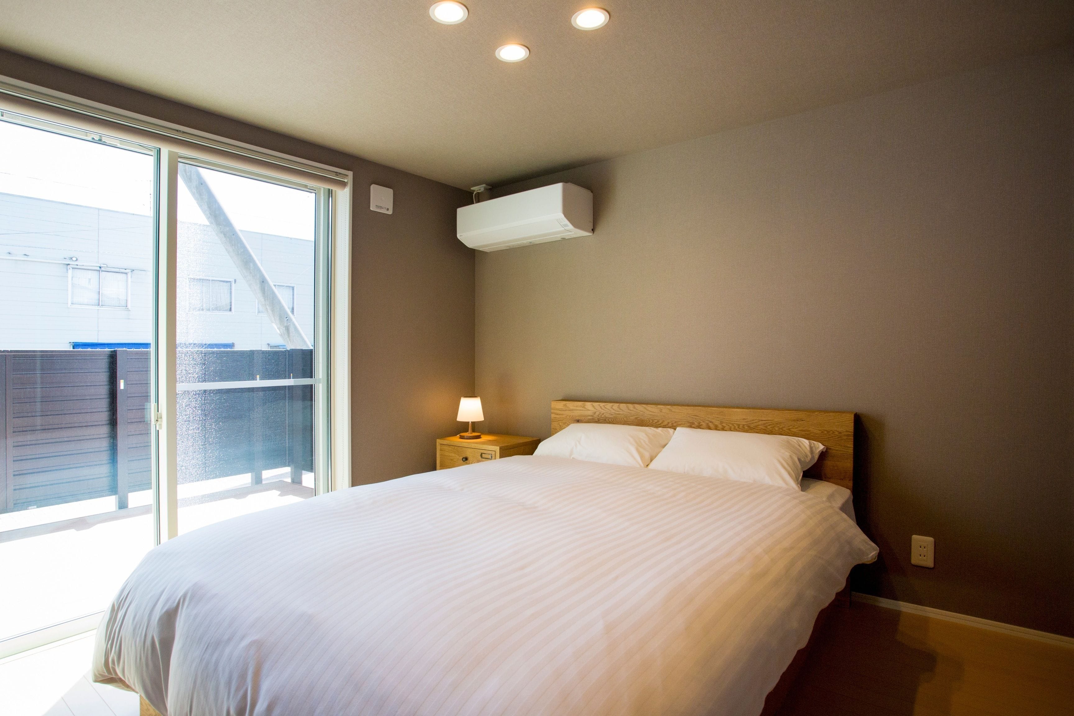 A bedroom with a bed, a nightstand, a lamp, an air conditioning unit, and a sliding glass door leading to an outdoor area.