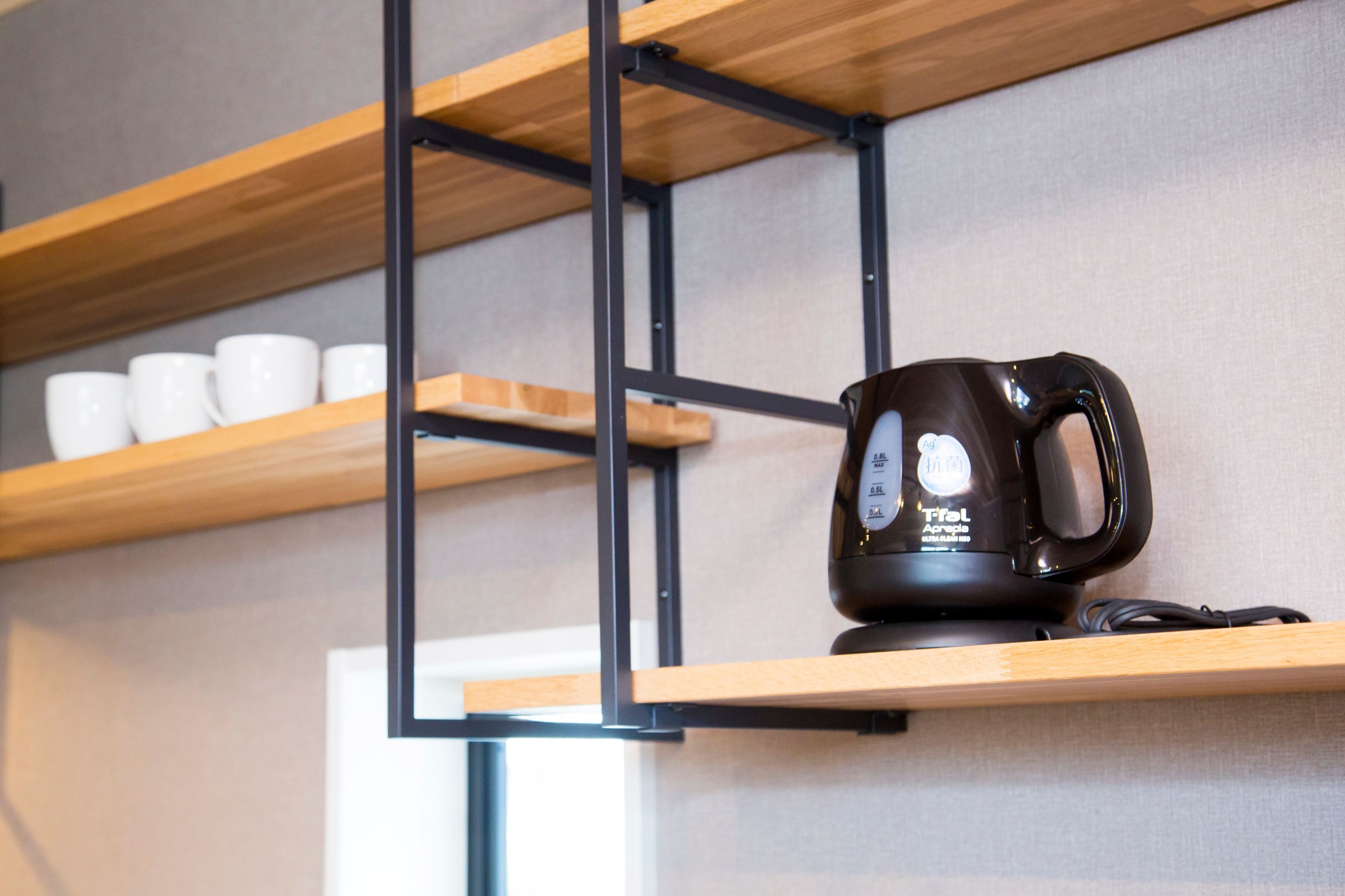 A coffee machine on a shelf with white cups in the background.