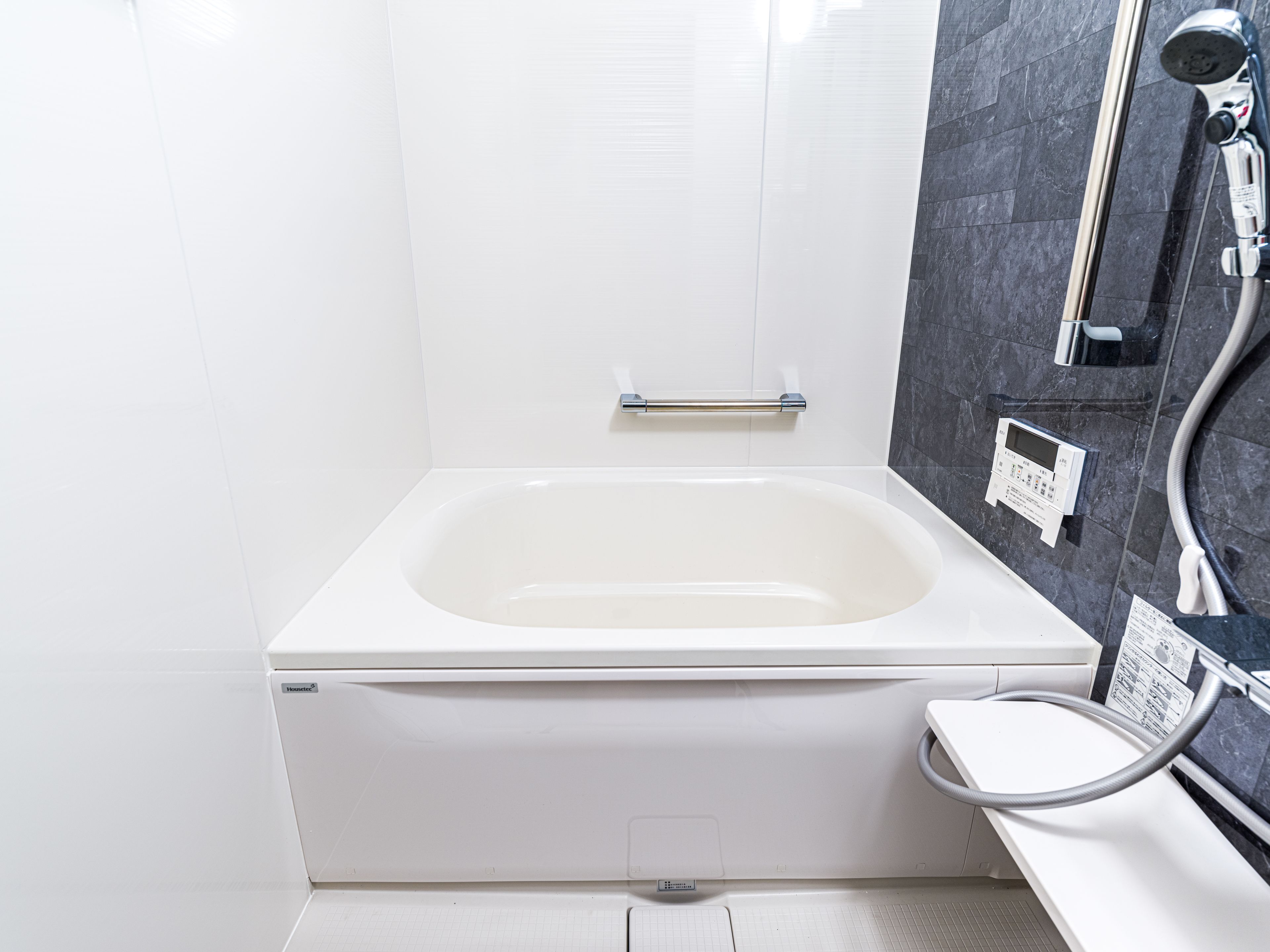 A modern bathroom with a white bathtub, a handheld showerhead, and a control panel on the wall.