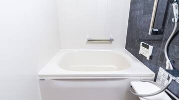 A modern bathroom with a white bathtub, a handheld showerhead, and a control panel on the wall.