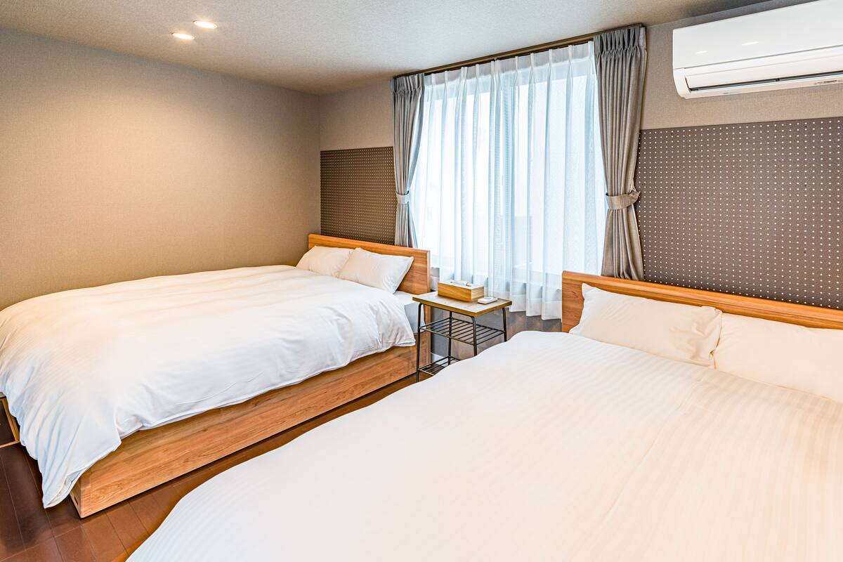 Habitación de hotel con dos camas, cabecero de madera, una mesita y equipo de aire acondicionado.