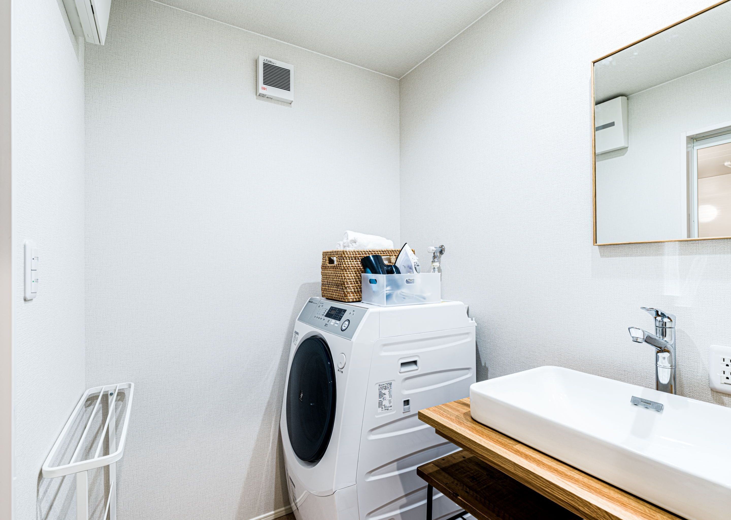 A compact laundry room with a washing machine, a drying rack, and a sink with a wooden countertop.