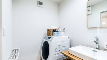 A compact laundry room with a washing machine, a drying rack, and a sink with a wooden countertop.