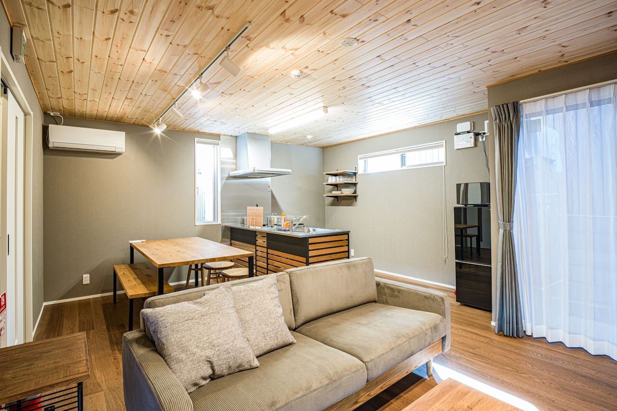 Un espacio habitable compacto con techo de madera, un sofá, una mesa de comedor y una kitchenette.