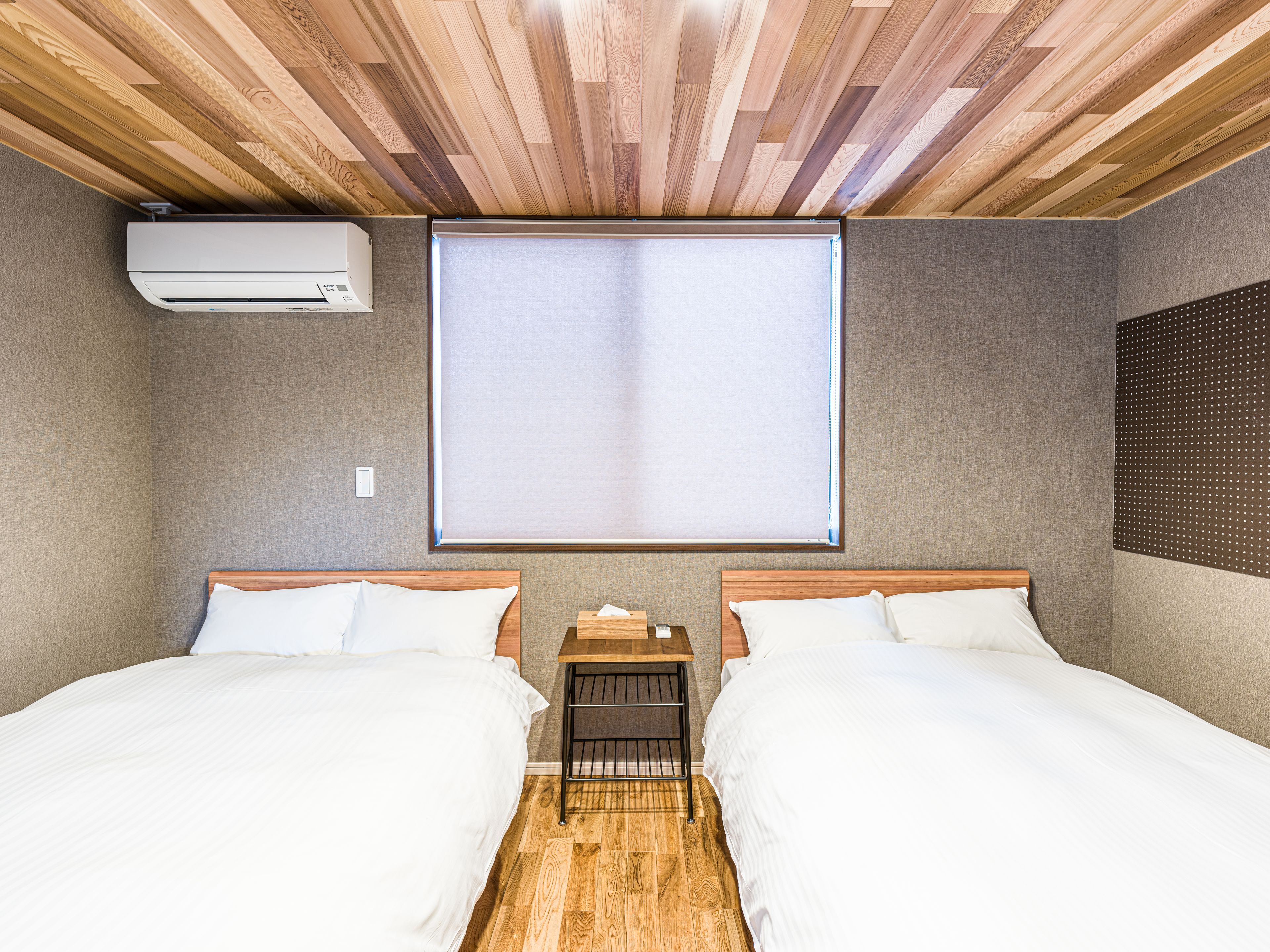 Une chambre d’hôtel avec deux lits, un ventilateur de plafond, une fenêtre avec des stores et un appareil de climatisation.
