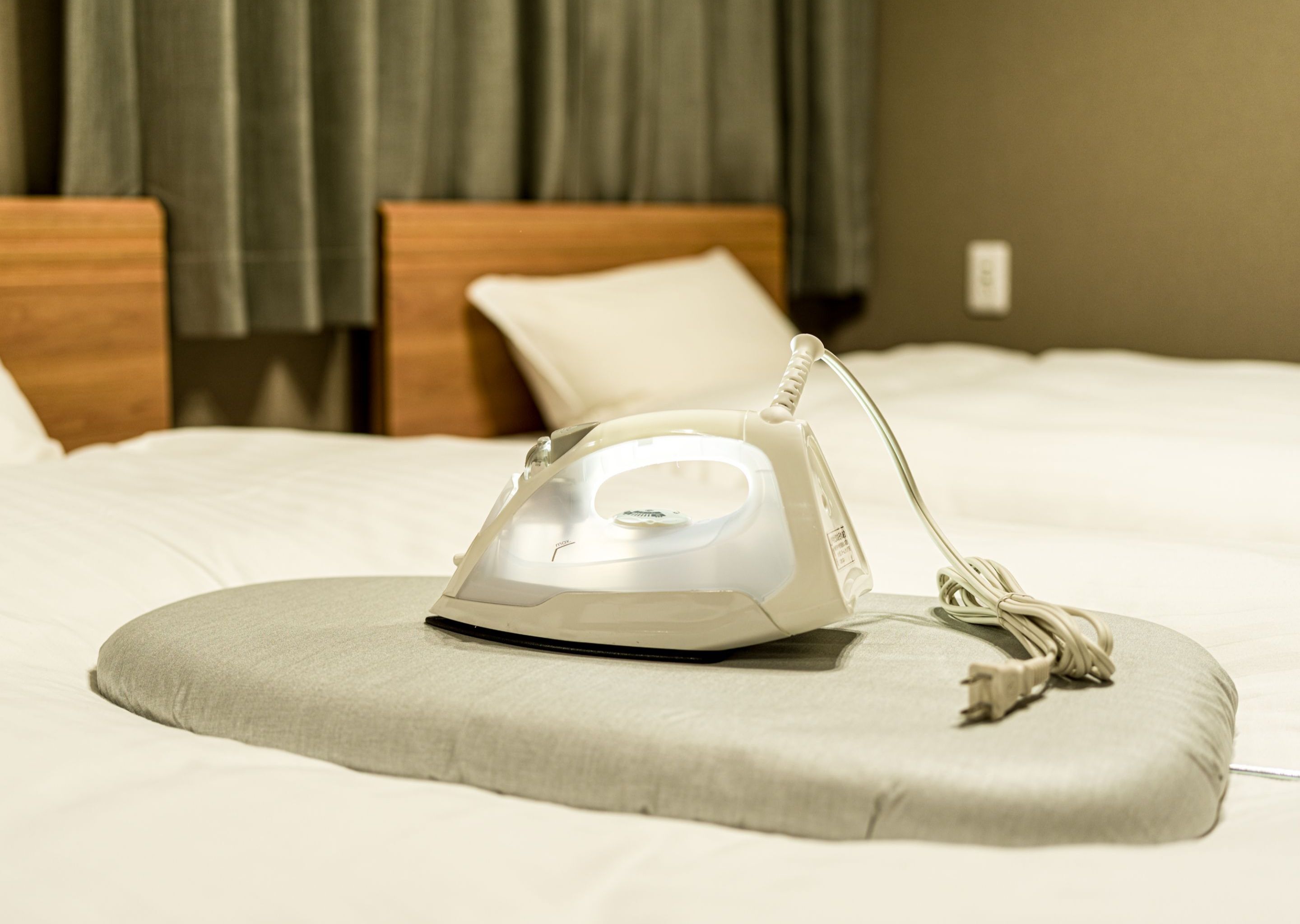 A bed with a white iron and a grey pillow.