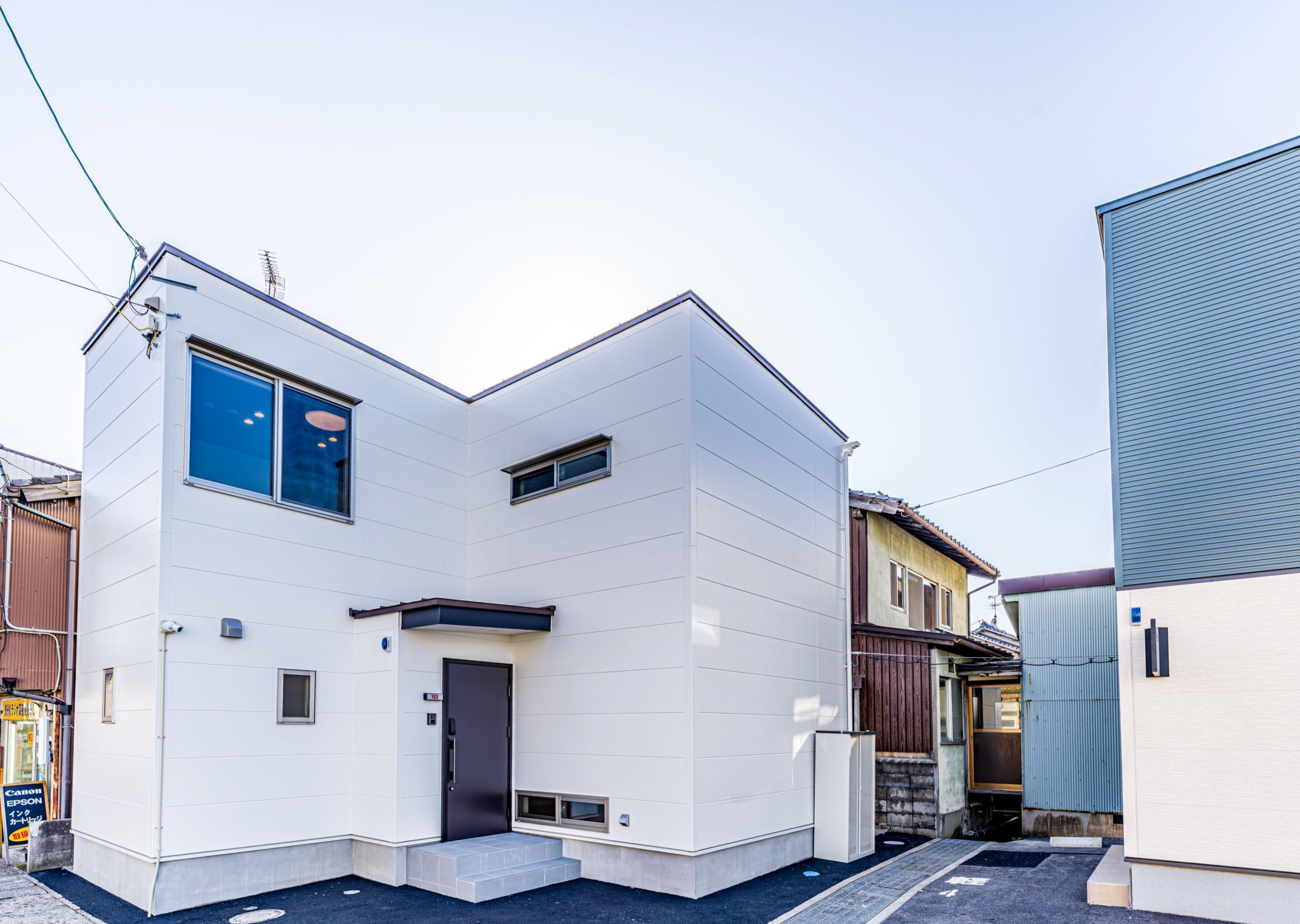 A modern two-story building with a flat roof, a small porch, and a visible door.