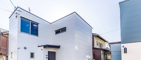 A modern two-story building with a flat roof, a small porch, and a visible door.