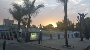 Una propiedad cercada con un cartel, una zona pavimentada y el atardecer al fondo.