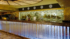 A hotel reception area with a decorative ceiling, a clock, and a water feature. - Grand Opera Hotel (Almaty)