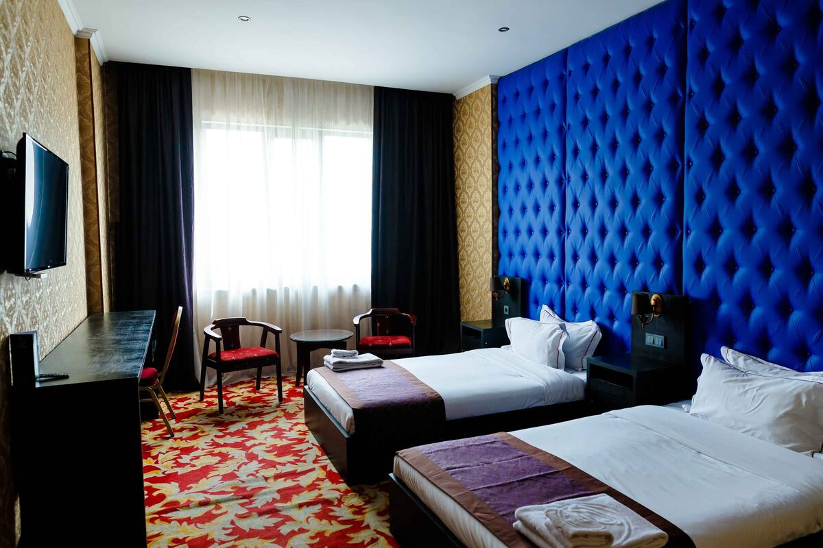 Une chambre d’hôtel avec deux lits, un bureau, une chaise, une télévision et une grande fenêtre avec des rideaux.