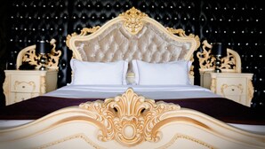 A luxurious bed with an ornate headboard, two nightstands, and a dark, studded wall. - Grand Opera Hotel (Almaty)