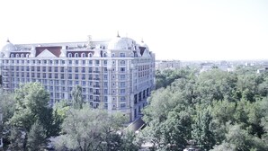 A large, multi-story building with a classical architectural style, surrounded by trees. - Grand Opera Hotel (Almaty)