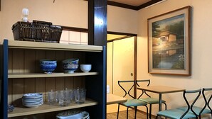 Ein Zimmer mit einem Holzbodenregal, das Schüsseln und Teller beherbergt, einem Esstisch mit Stühlen und einem gerahmten Gemälde an der Wand.