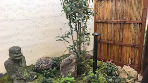 Ein Garten mit einer Steinstatue, einem Bambuszaun und verschiedenen Pflanzen.