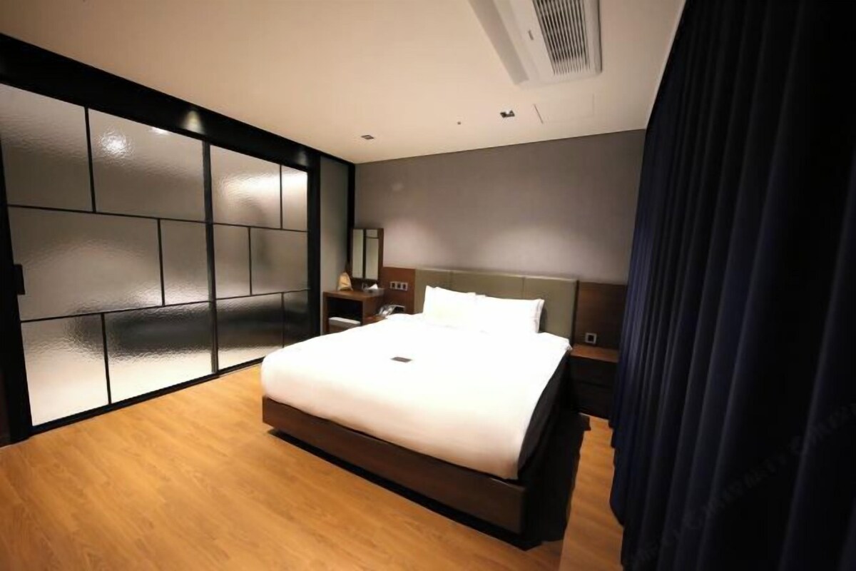A modern hotel room with a large bed, a nightstand, a mirror, and a dark curtain.
