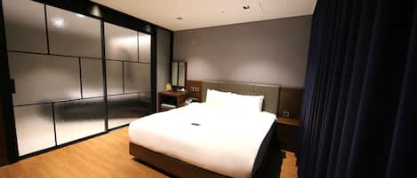 Een moderne hotelkamer met een groot bed, houten vloer, een inbouwkast en een nachtkastje.