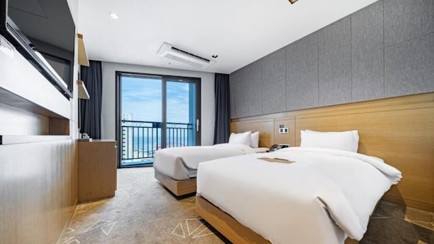 A hotel room with two beds, a balcony, and a view of the city. - Sea Cruise Hotel (Sokcho)