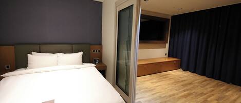 Habitación de hotel con cama, mesita de noche y un amplio ventanal con cortinas.