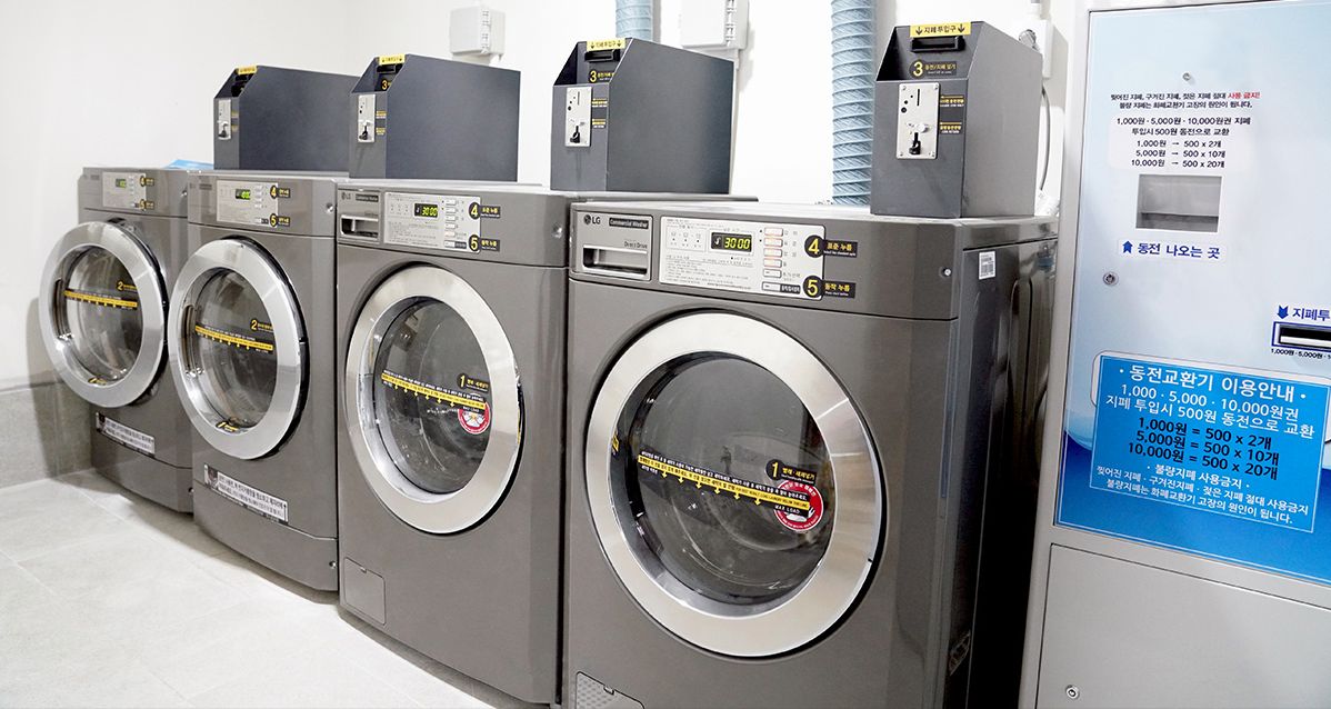 Een rij commerciële wasmachines met bedieningspanelen en een prijslijst.