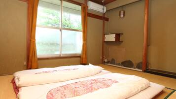 Une pièce de style japonais traditionnel, avec un sol recouvert de tatamis, un futon servant de lit, une porte coulissante et une vue sur un jardin.
