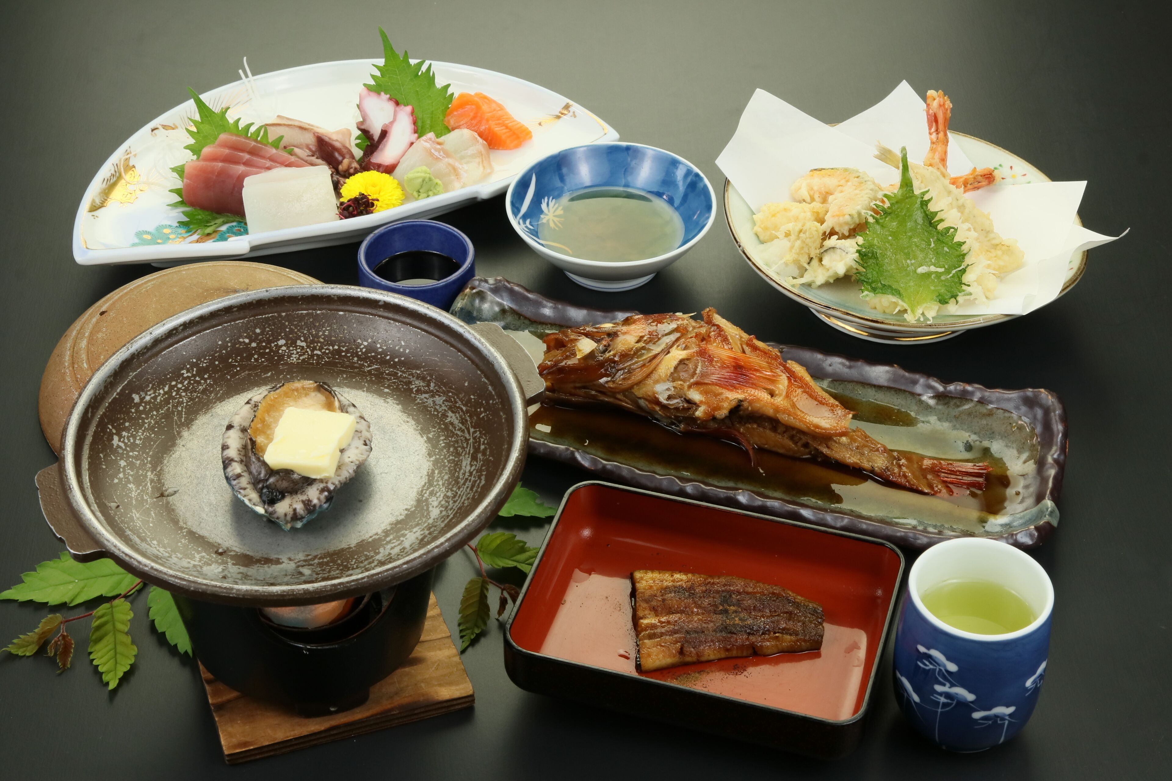 A variety of Japanese dishes including sashimi, grilled fish, and shrimp, served on different plates and bowls.