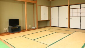 Una habitación japonesa tradicional con suelo de tatami, televisor y puertas correderas.