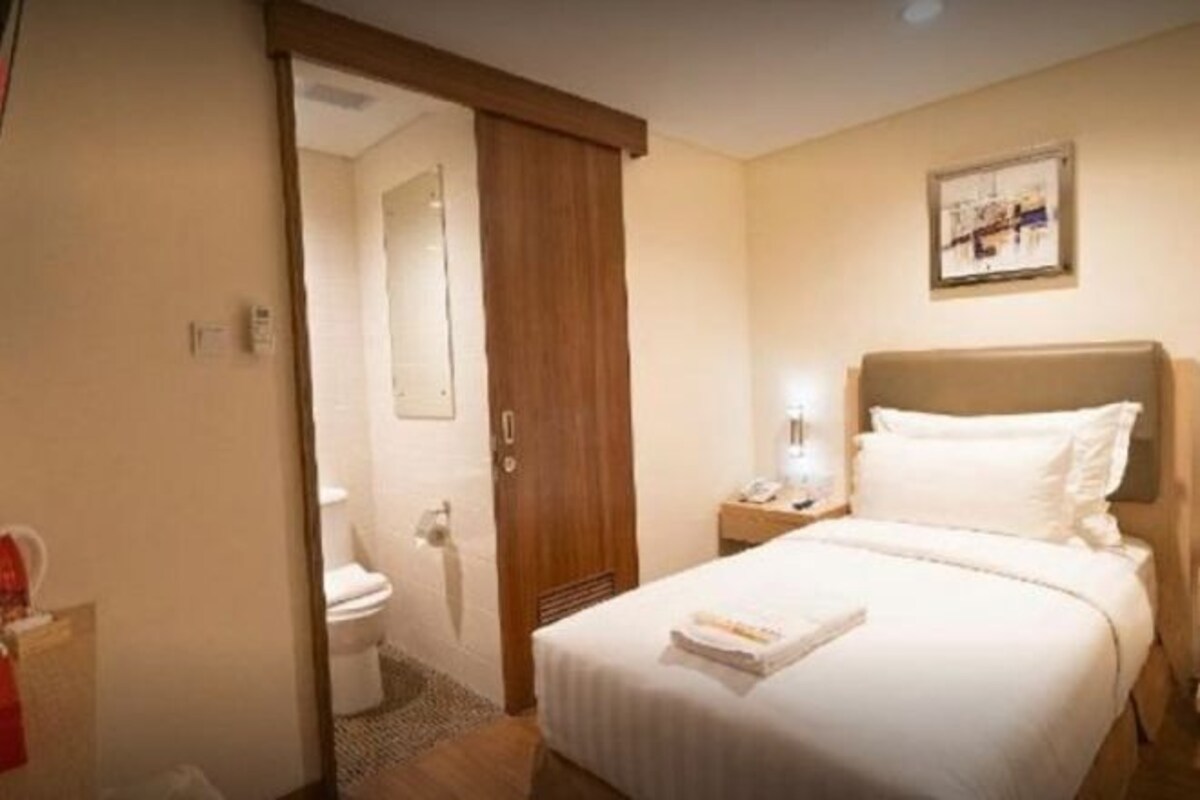 Quarto de hotel com uma cama, mesa de cabeceira, quadro na parede e porta de acesso a um banheiro.