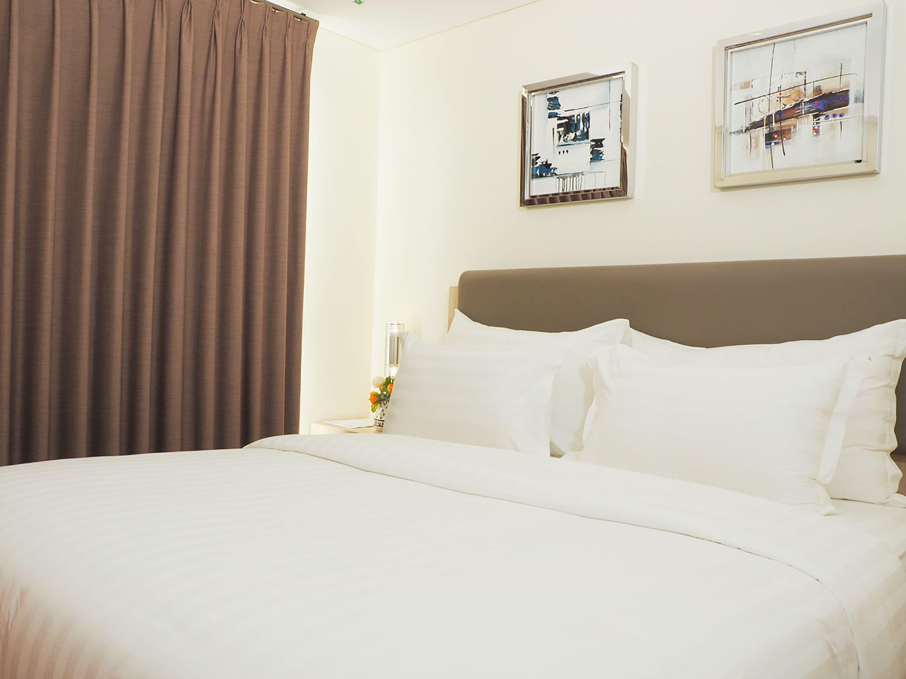 A hotel room with a large bed, a headboard, two framed artworks on the wall, and a curtain.