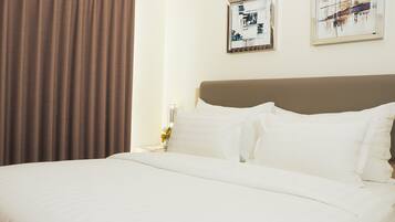 A hotel room with a large bed, a headboard, two framed artworks on the wall, and a curtain.