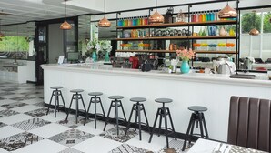 Zona de bar moderna con mostrador blanco, taburetes negros y una variedad de vasos de colores en estanterías.
