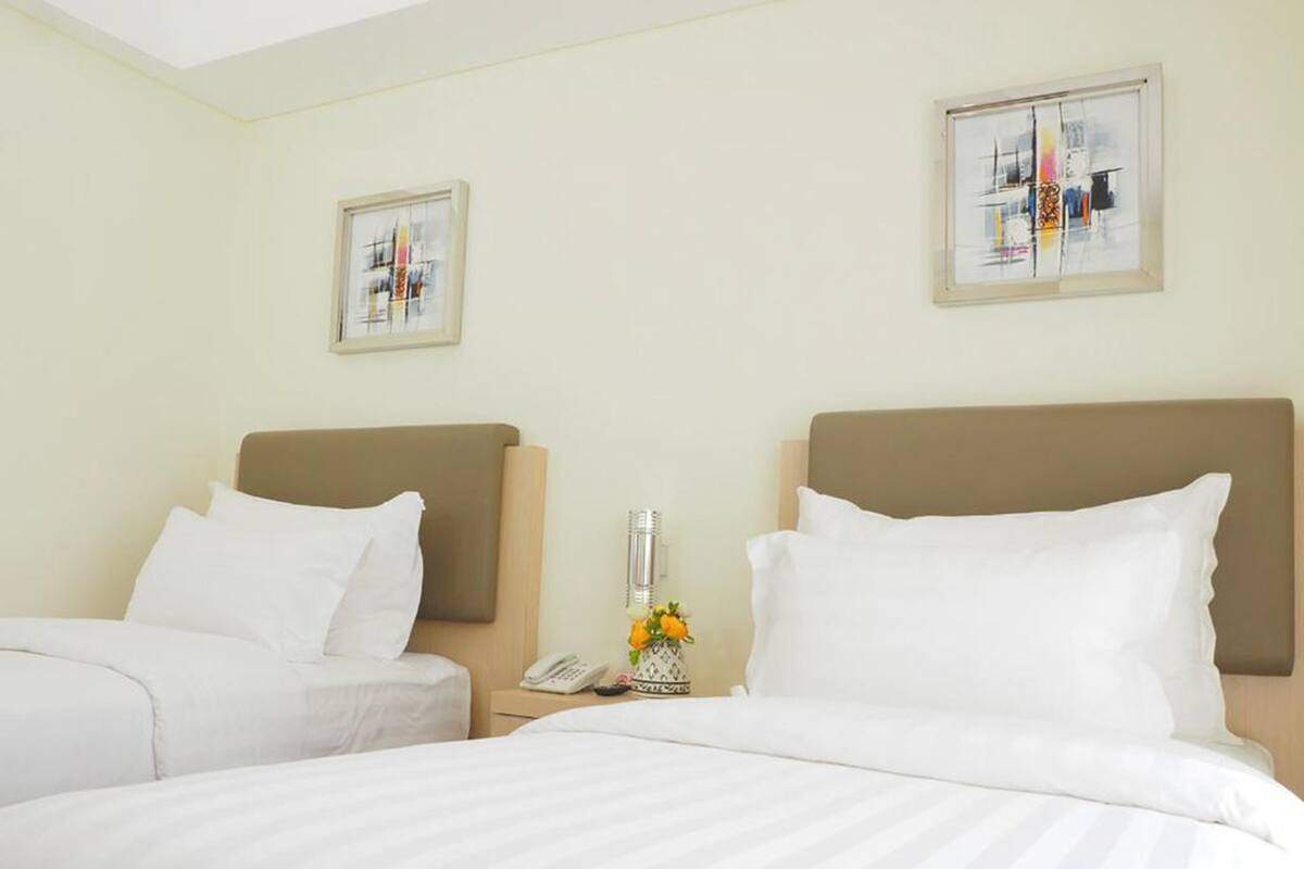 Habitación de hotel con dos camas, una mesita de noche con un teléfono y un florero, y dos obras de arte enmarcadas en las paredes.