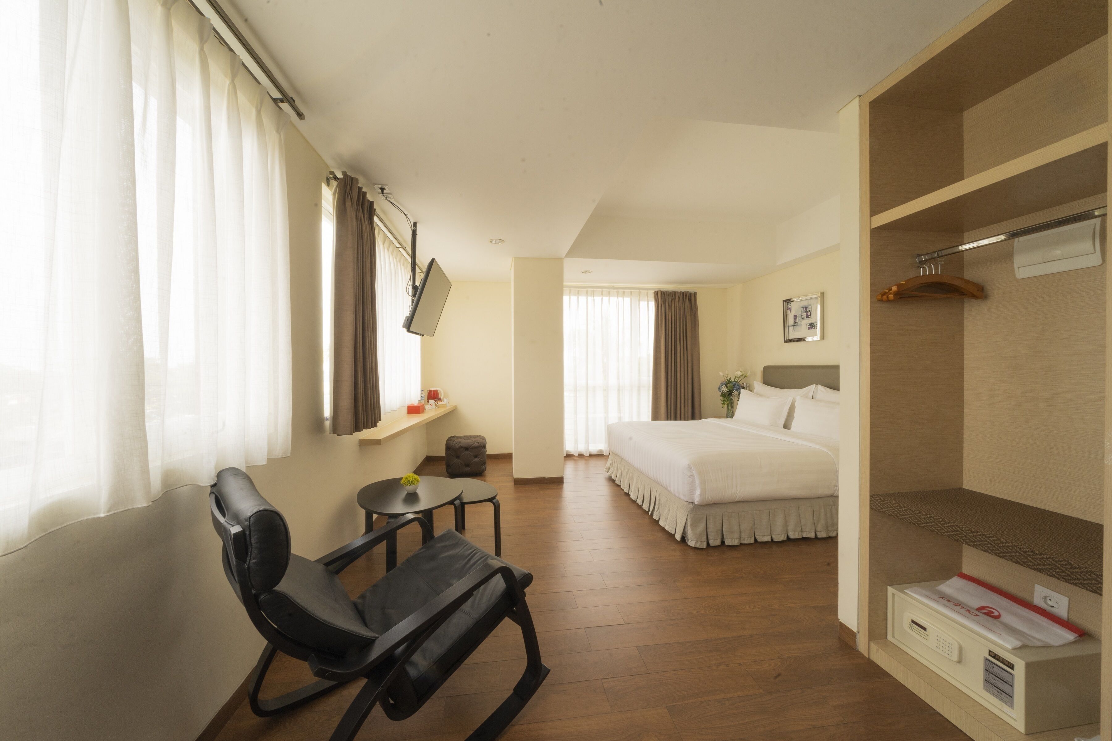 Quarto de hotel com cama, escrivaninha, cadeira, guarda-roupa e janela com cortinas.