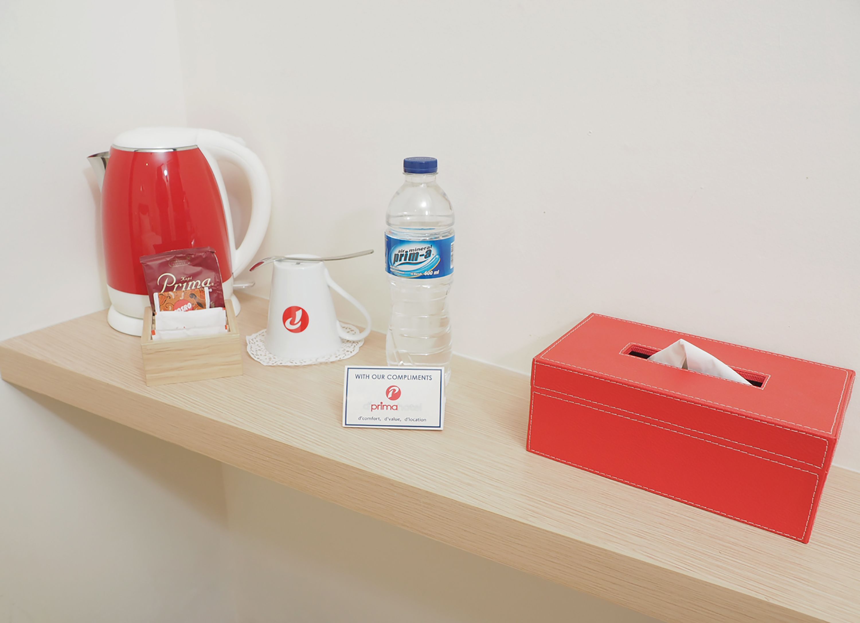 A wooden counter with a red kettle, a water bottle, a tissue box, and a sign with the Prima logo.