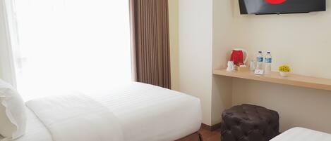 A hotel room with two beds, a TV mounted on the wall, a shelf with toiletries, and a window with curtains.