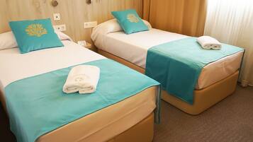 Two twin beds with teal bedspreads and matching pillows, a white towel on each bed, and a wooden headboard.