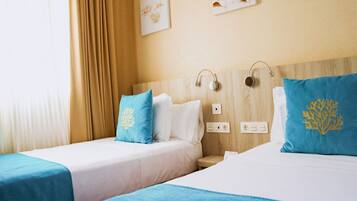 Habitación de hotel con dos camas, cada una con colcha azul y almohadas a juego. Hay enchufes en la pared y un cabecero con altavoces integrados.