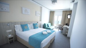 A hotel room with a large bed, a desk, a chair, and a view of the sea. - Hotel Sol de Jávea (Javea)