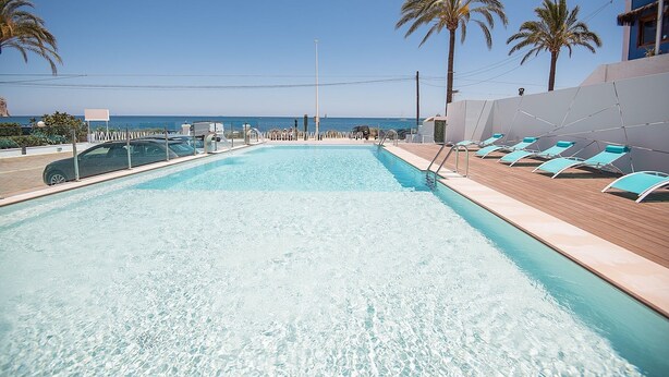 A pool with clear water, surrounded by lounge chairs and palm trees, with a view of the sea. - Hotel Sol de Jávea (Javea)