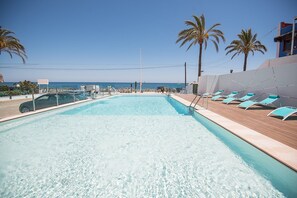 A pool with clear water, surrounded by lounge chairs and palm trees, with a view of the sea. - Hotel Sol de Jávea (Javea)