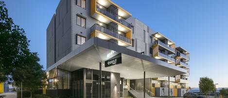 A modern hotel with a covered entrance, multiple balconies, and a sign reading "QUEST".