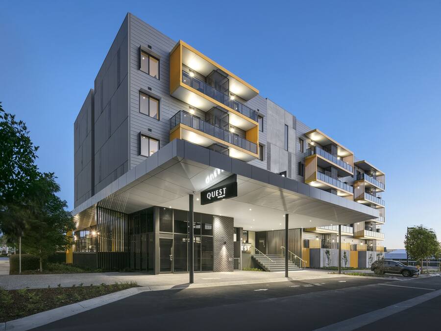 A modern hotel with a covered entrance, multiple balconies, and a sign reading "QUEST".