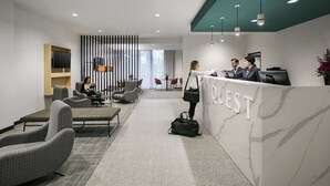 A modern reception area with a marble counter, seating, and a large TV screen. - Quest Notting Hill (Notting Hill)