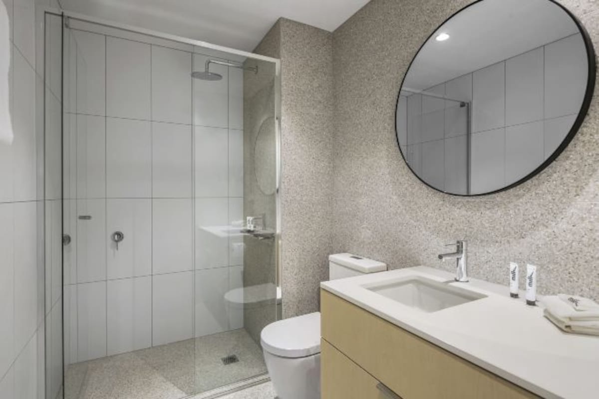 A modern bathroom with a glass-enclosed shower, a toilet, a sink with a mirror, and a towel on the counter.